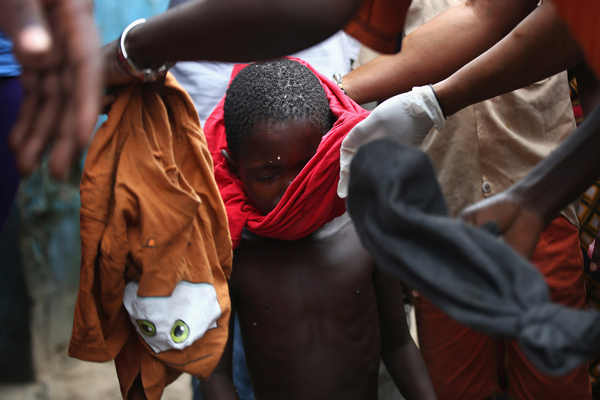 Residents dress Saah Exco, 10, after bathing him. According to a community organiser, Saah's mother died of suspected but untested Ebola in West Point before he was brought to the isolation centre with his brother, Tamba, 6, aunt Ma Hawa, and cousins. His brother died on August 15. Saah fled the centre with several other patients before it was overrun on August 16 by a mob. Once out in the neighbourhood, he was not sheltered, as he had suspected Ebola - so he has been sleeping outside. The whereabouts and condition of his aunt and cousins, who left the facility when it was overran by the crowd, is still unknown