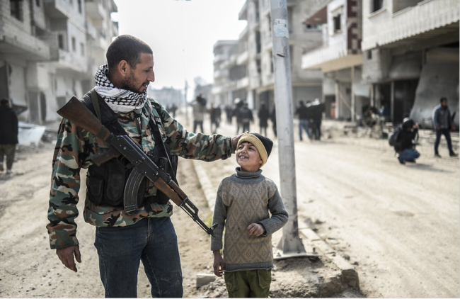 A Kurdish fighter walks with his child in the streets of Kobani, Syria after they recaptured it from ISIS militants.