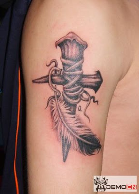 cross tattoo on the arm with a feather close by.