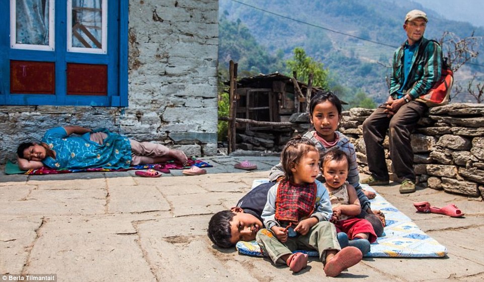 Four Nepalese hildren play on their mat while a woman naps behind on rug in the mid-day sun