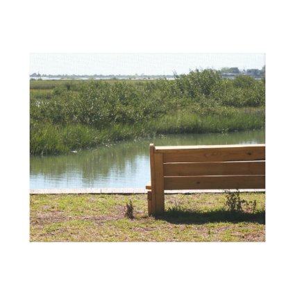 Bench by river with grass and water canvas print