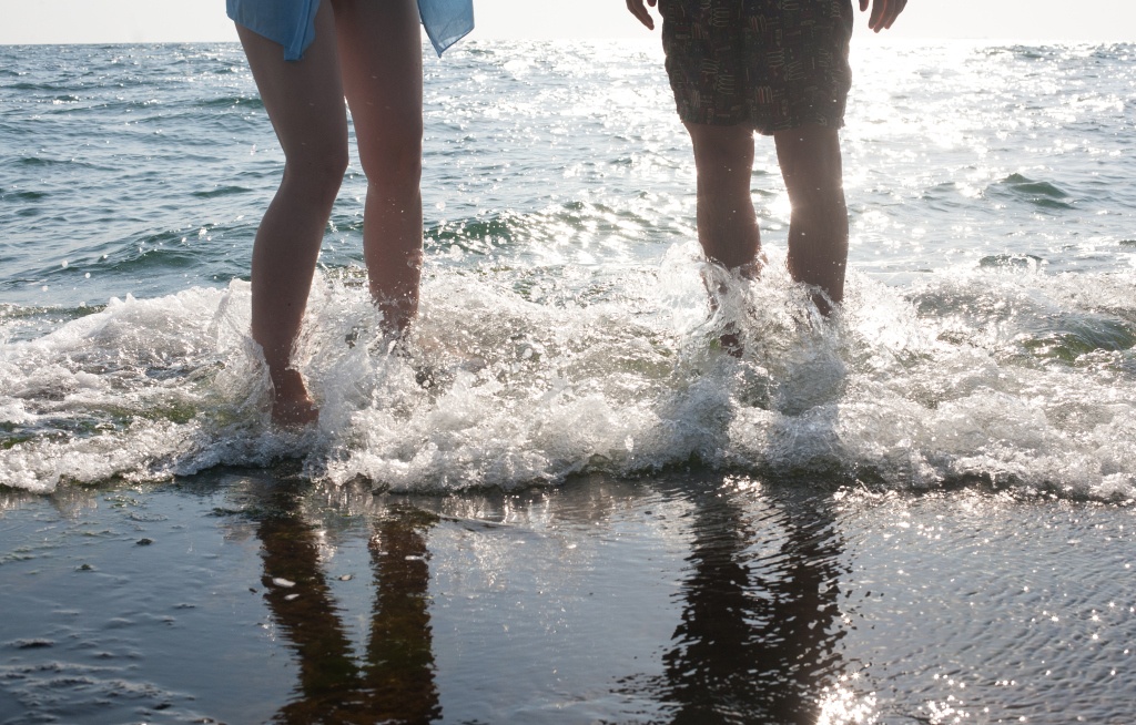 legs of two people standing in the sea-foam