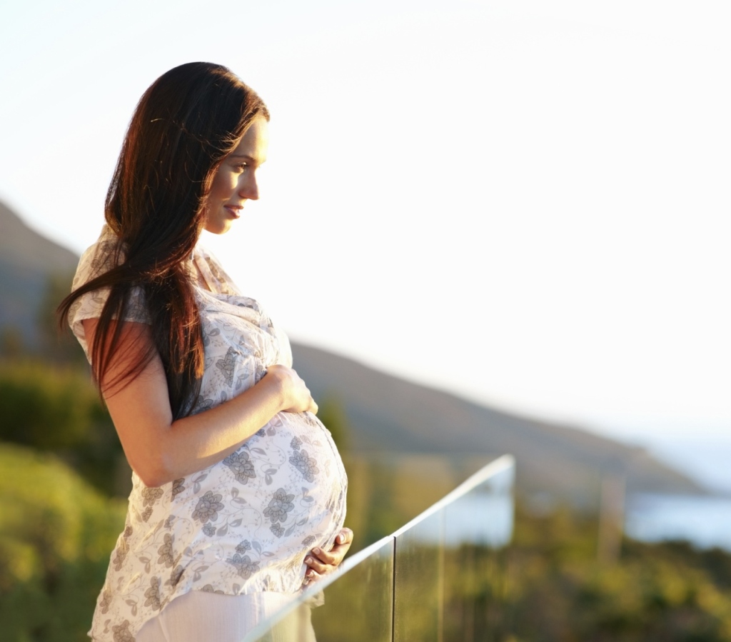 Side view of a pregnant young woman outdoors on a sunny day - copyspace