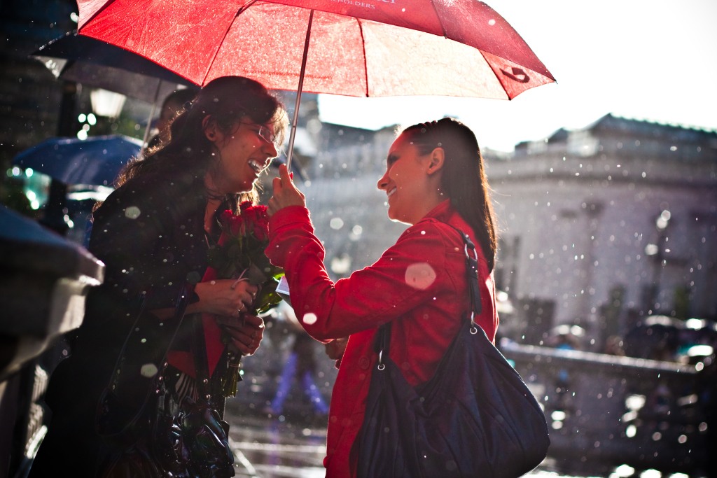 Two women meet up in the rain at London's Trafalgar Square.