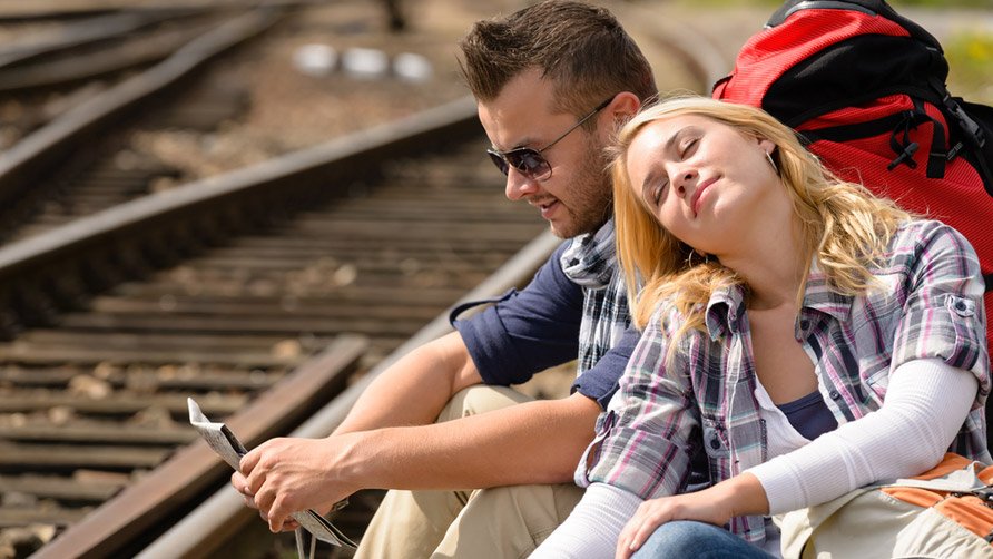 couple-backpack-traveling-resting-on-railroad-map-happy