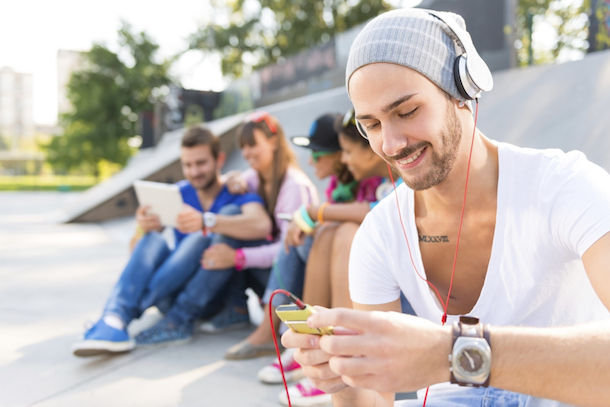Young guy in the skate park with headphones looking at smartphone