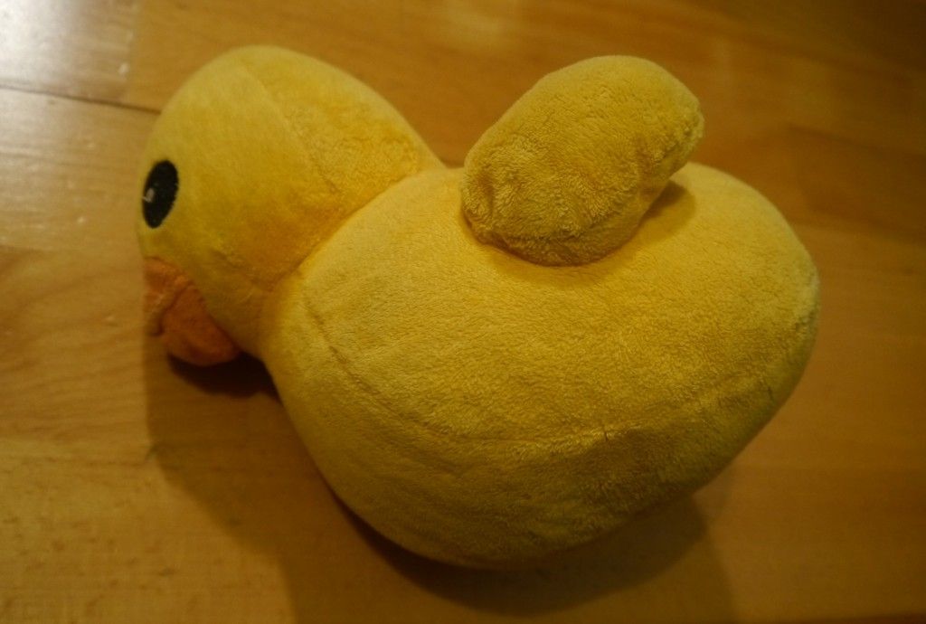 A photo of a cuddly toy yellow duck which has fallen over onto its side