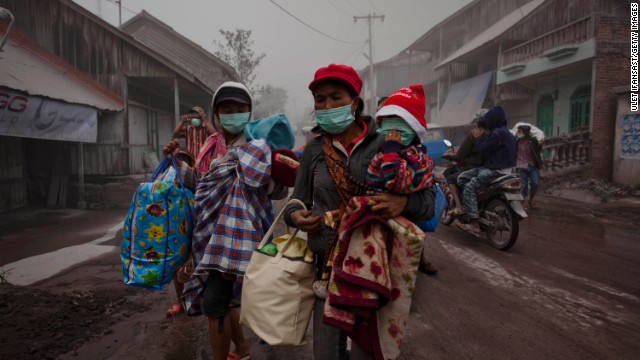 Women evacuate with their children to a temporary evacuation center on January 8 after their village is hit by ash.