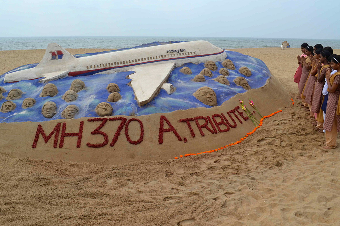 Schoolgirls pray next to a sand sculpture created by sand artist Sudarshan Patnaik to pay tribute to passengers and crew onboard the missing Malaysia Airlines flight MH370, on a beach in Puri, in the eastern Indian state of Odisha