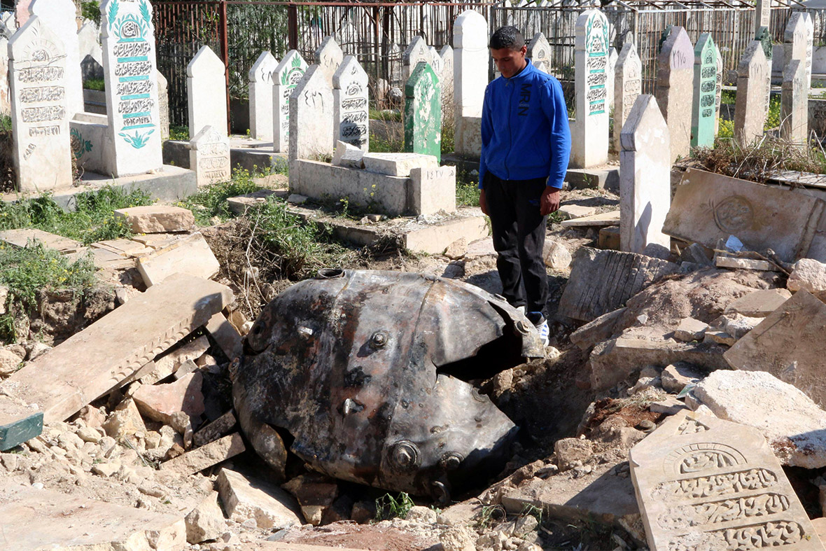 A man looks down at an unexploded barrel bomb dropped by forces loyal to Syria's President Bashar al-Assad at a cemetery in the al-Qatanah neighbourhood of Aleppo