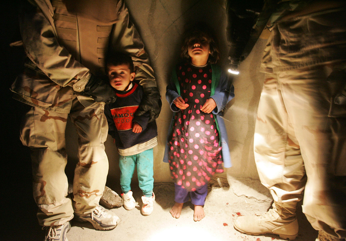 January 18, 2005: Two children are held by US soldiers after their parents were killed when their car was fired on by US troops for failing to stop in Tal Afar, Iraq. Six children in the in the car survived, one with a flesh wound