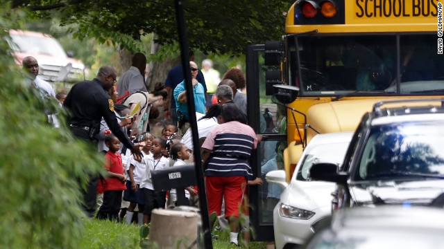 A police officer interacts with students as they board school buses to take them to reunite with their parents. 