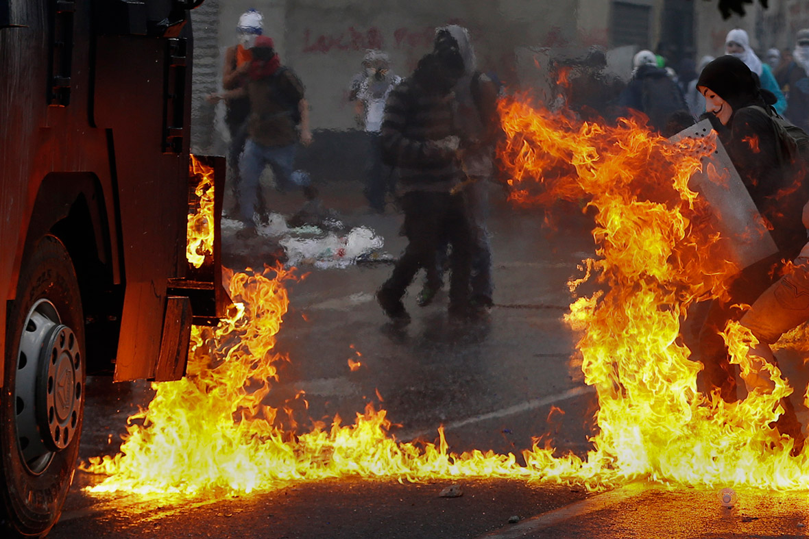 An anti-government protester wearing a Guy Fawkes mask is surrounded by flames from Molotov cocktails thrown at a water cannon