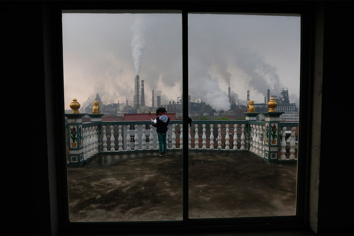A girl reads a book on her balcony as smoke rises from chimneys at a nearby steel plant, on a hazy day in Quzhou, Zhejiang province, China