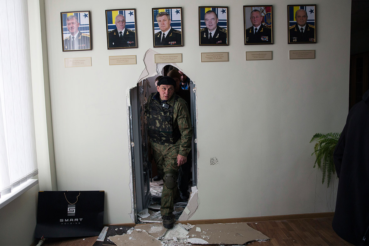 A member of pro-Russian forces looks through a wall after breaking into the naval headquarters in Sevastopol