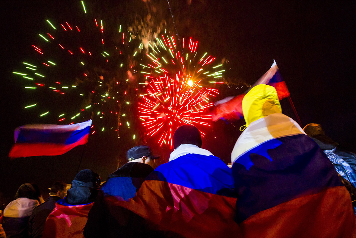 People wrapped in Russian flags watch as celebratory fireworks explode after the preliminary results of the referendum are announced on Lenin Square in Simferopol