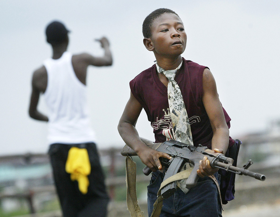 July 30, 2003: A child soldier loyal to the Liberian government walks away from firing on rebel forces across a key bridge in Monrovia, while another taunts them