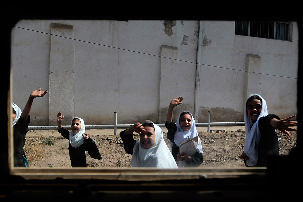June 26, 2010: Afghan schoolgirls, seen through the window of a Humvee, wave to a passing American convoy in Herat