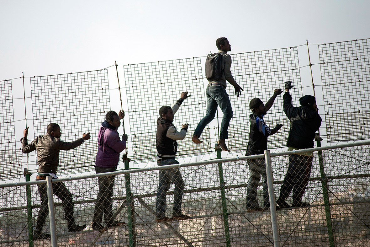 African migrants climb a border fence covered in razor wire during an attempt to cross into Spanish territory between Morocco and Spain's north African enclave of Melilla