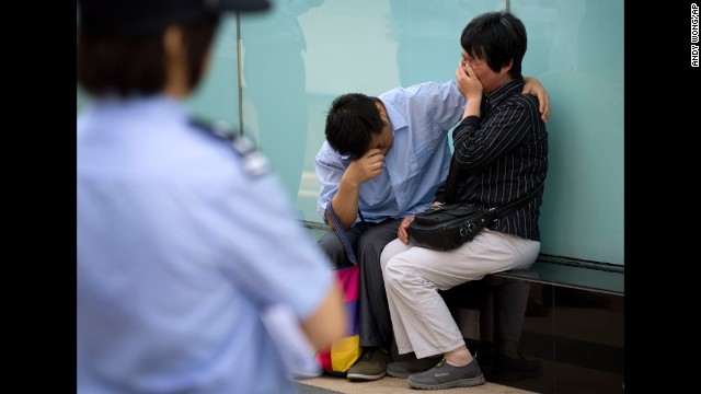 A policewoman watches a couple whose son was on board the missing Malaysia Airlines Flight 370 cry outside the airline's office building in Beijing after officials refused to meet with them on Wednesday, June 11. The jet has been missing since March 8.