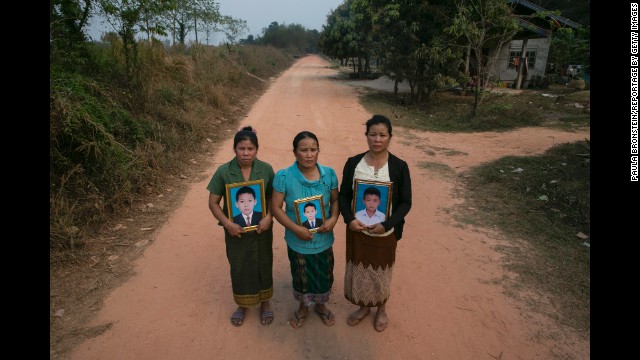 Three mothers hold framed portraits of their sons on the same dirt road in Laos where they were killed in January. The children found a cluster bomb and started playing with it like it was a toy.