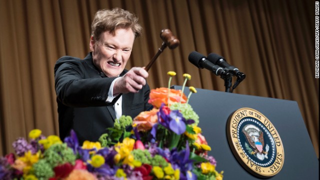 Conan O'Brien bangs a small gavel on the podium during his performance.