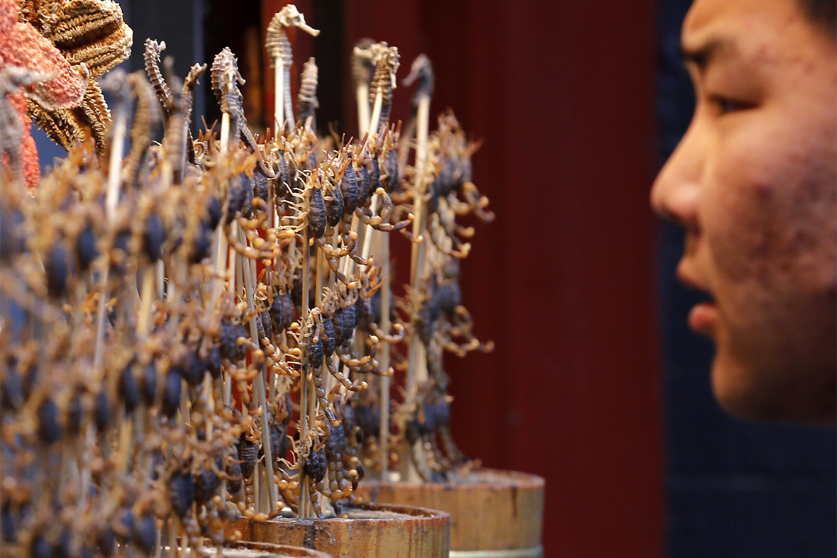 A man looks at deep-fried scorpions and seahorses displayed for sale at a food stall in Beijing