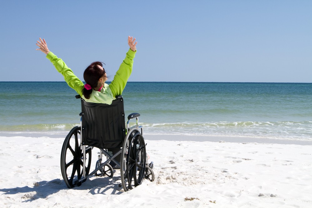Woman with arms raised celebrates her achievement and success in the sunshine even with her disabilities in a wheelchair.