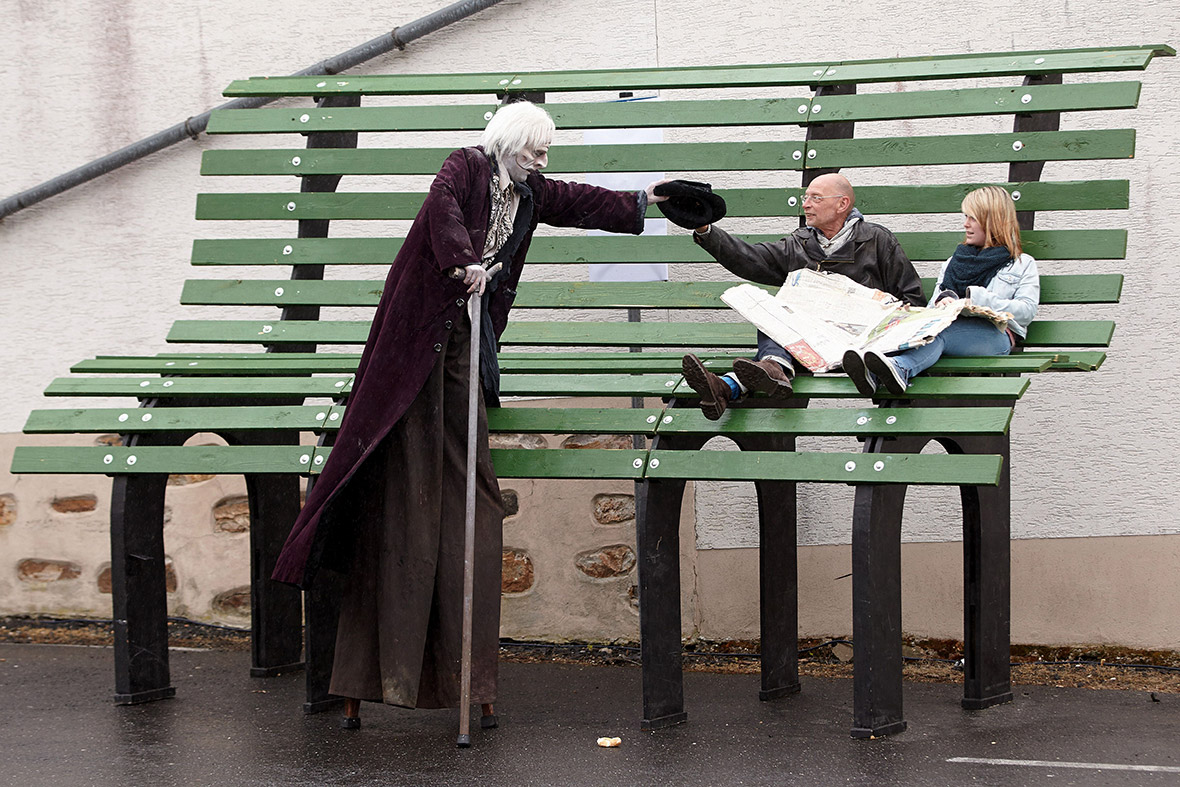 An actor on stilts walks past a giant park bench during a Theatre Somente performance in Hachenburg, Germany.