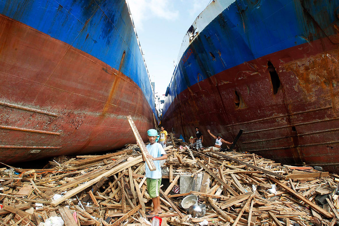 November 11, 2013: Residents pick up pieces of wood inbetween two cargo ships that were washed ashore when super typhoon Haiyan hit Anibong town, Tacloban