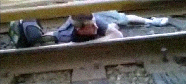 Crazy kid crawls across the railway tracks under a running train