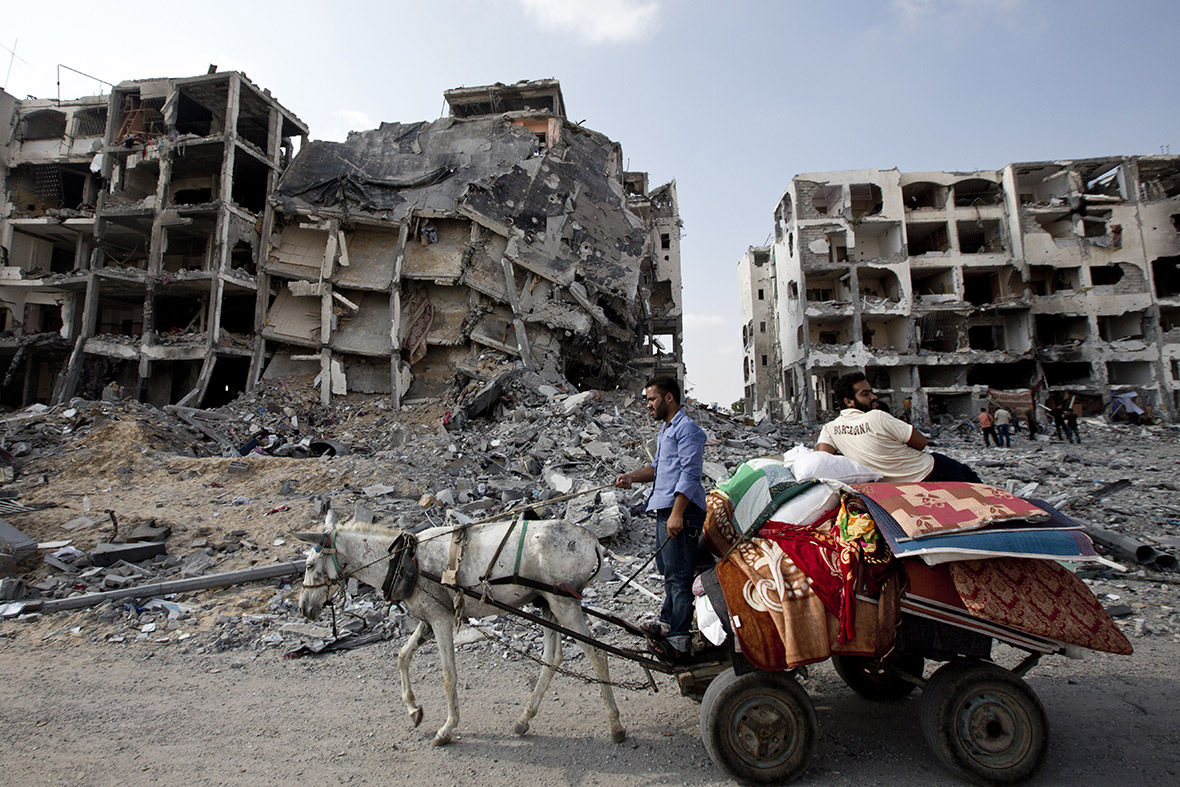 Palestinian men ride a donkey cart past destroyed buildings in the northern Gaza Strip, as a 72-hour humanitarian truce went into effect