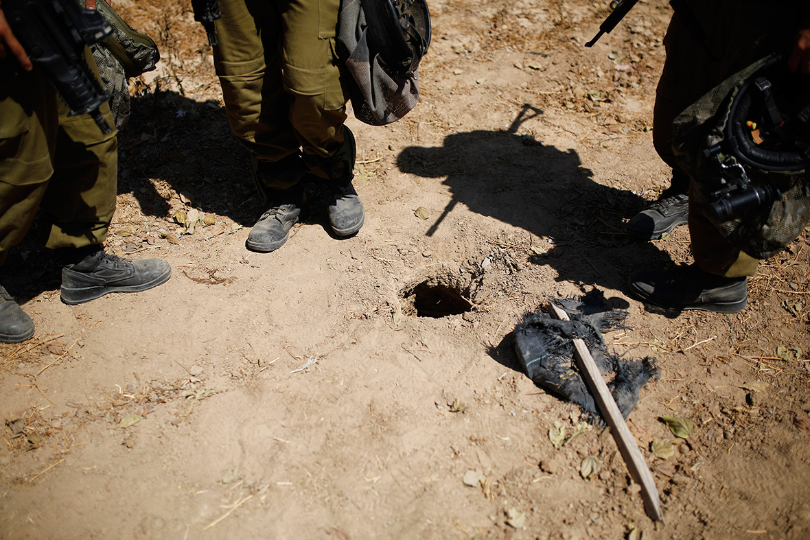 Israeli soldiers stand over a hole in the ground they suspect is connected to a tunnel, outside the Gaza Strip