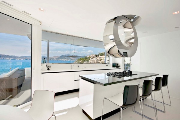 A highly contemporary chrome extractor design is the star of the show in this slick ice-white kitchen with sharp black trims. The central cooking island also doubles a casual eating area for four diners.