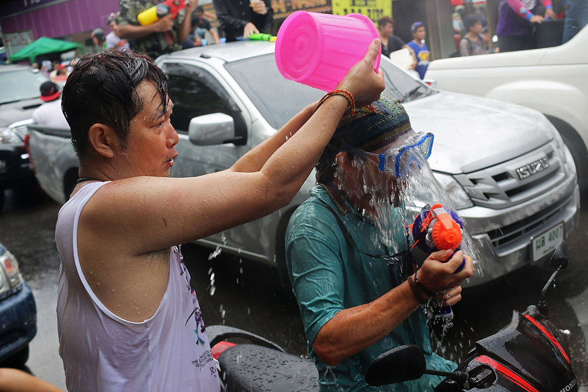 A Thai man pours a bucket of water on a man riding a scooter in Chiang Mai