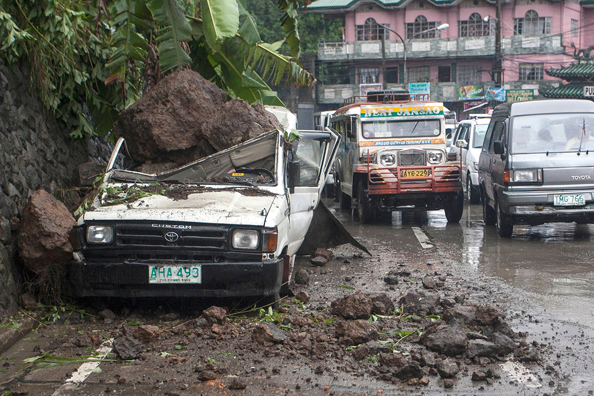 Motorists drive past a parked vehicle damaged by a landslide due to monsoon rains brought by Typhoon Ester in Baguio, the northern Philippines