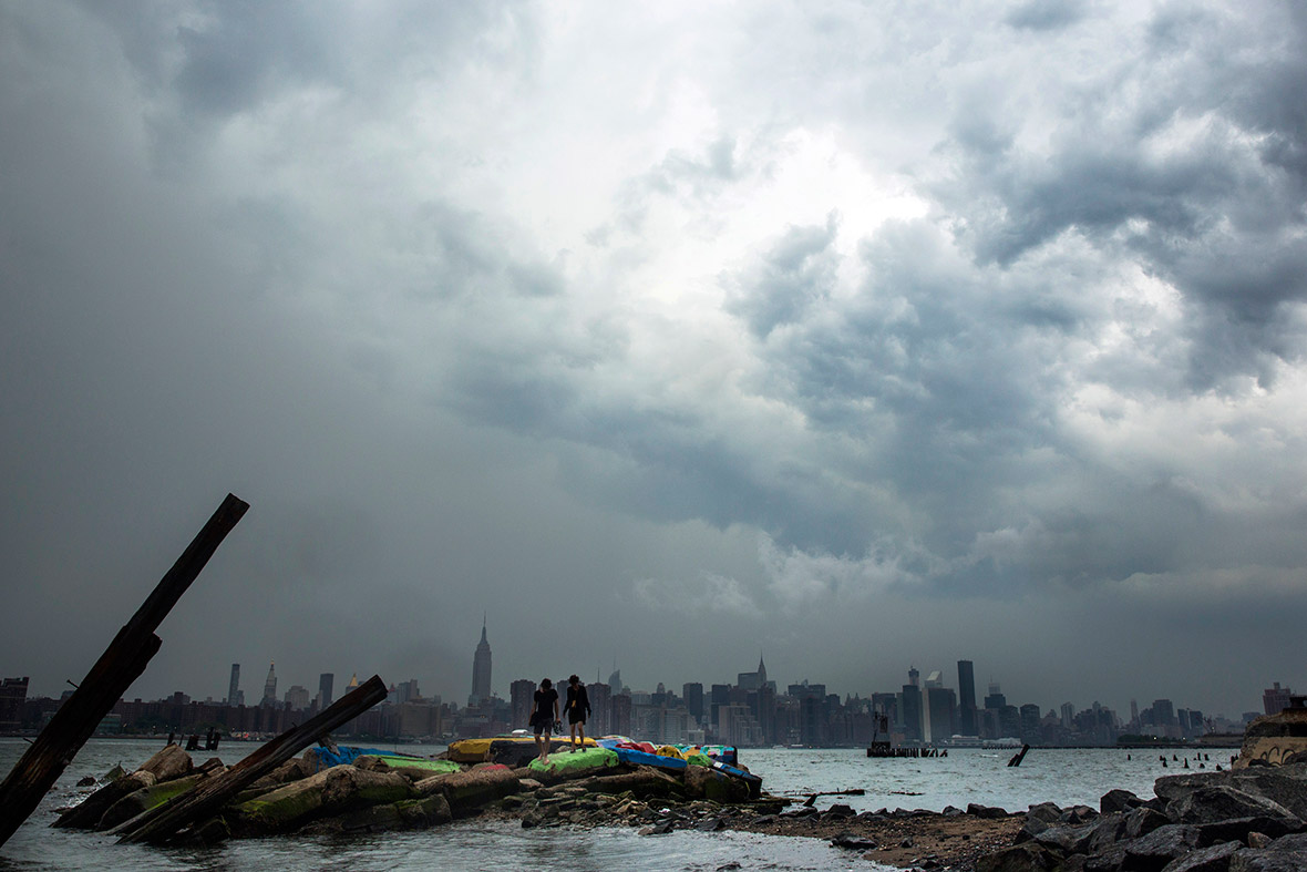 Two people walk on painted rocks, as a large storm looms over the skyline of New York
