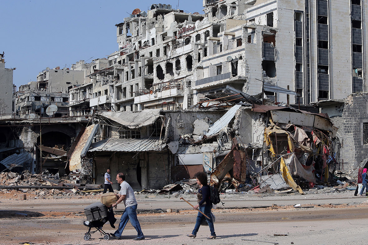 Syrians carry their belongings past destroyed buildings