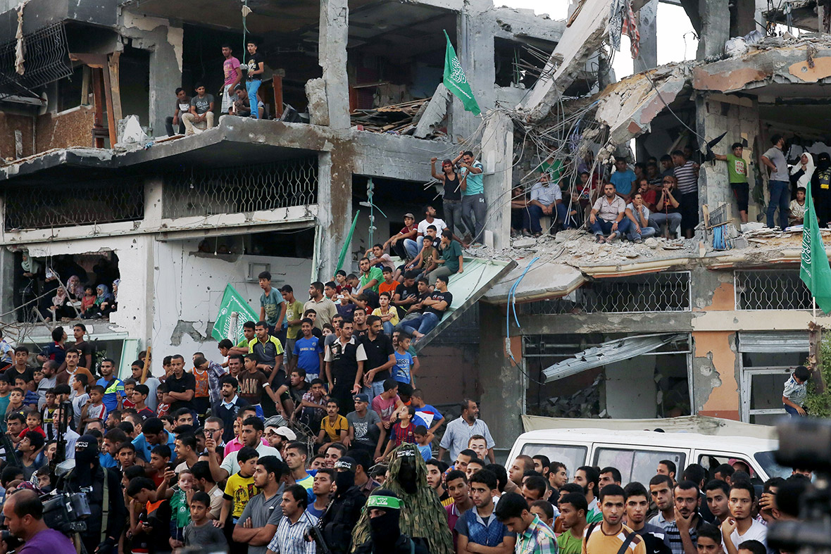 Palestinians stand in the rubble of a building that was destroyed during fighting between Hamas militants and Israel, as they watch a parade by Hamas militants in Shejaiya.