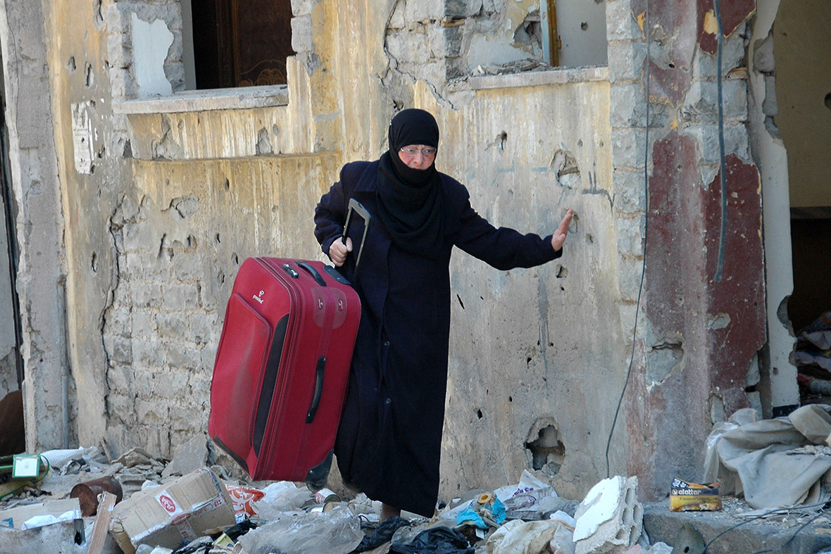 A woman carrying a suitcase picks her way through the rubble in the Juret al-Shayah district