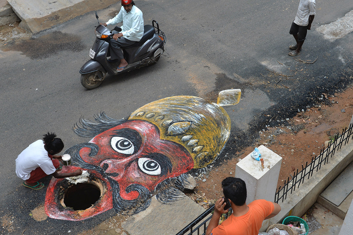 Indian artist Badal Nanjundaswamy uses the opening of an unattended manhole in the middle of a road to depict the Hindu God of death 'Yama' waiting to gobble up unwary pedestrians or motorists in Bangalore.