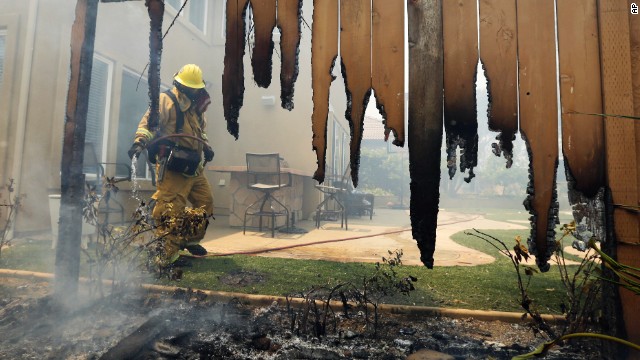 A firefighter puts water on a smoldering fence outside a home in Carlsbad on May 14. The wildfire in Carlsbad is about 20 miles away from a wildfire in San Diego that has burned more than 1,500 acres.