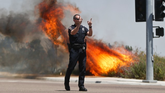 A Carlsbad police officer turns traffic away as flames rage behind him on May 14.