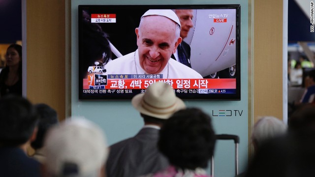 People watch Pope Francis' arrival on a television at the Seoul Railway Station.