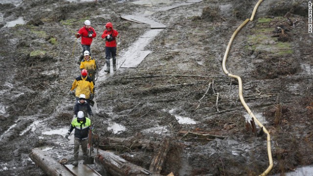Search-and-rescue teams use a path of plywood to walk through a muddy field in Arlington, Washington, on Sunday, March 30.