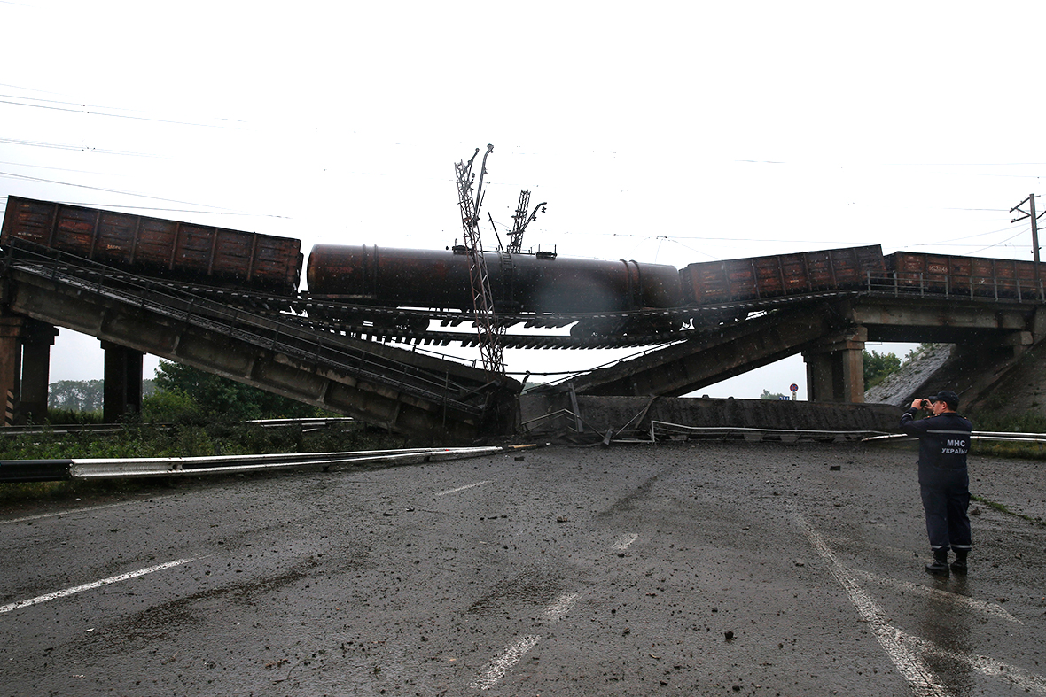 A member of the Ukrainian emergency services takes a photograph of a destroyed rail bridge which fell over a main road leading to the eastern Ukrainian city of Donetsk