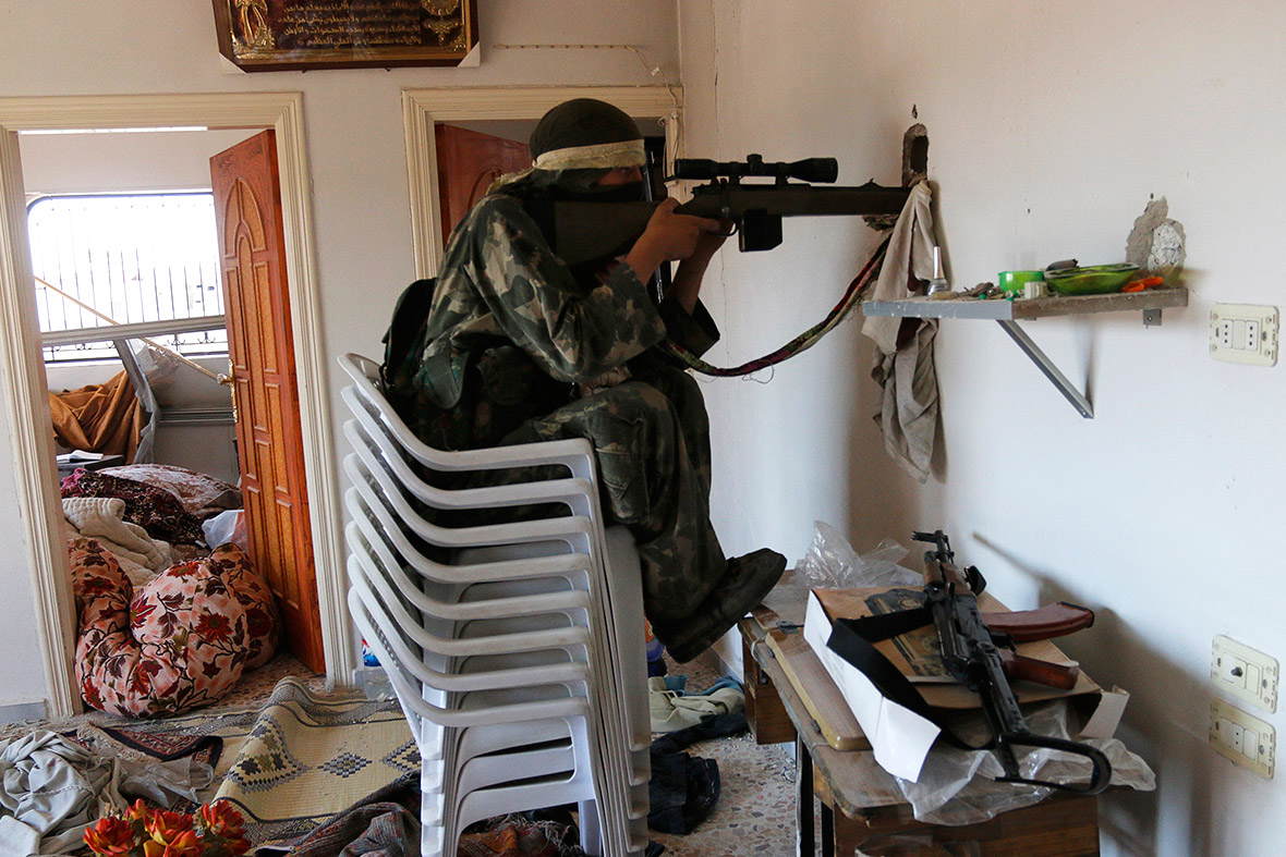 A rebel fighter sits on stacked chairs as he aims his weapon through a hole inside a house in the town of Morek in Hama province, Syria