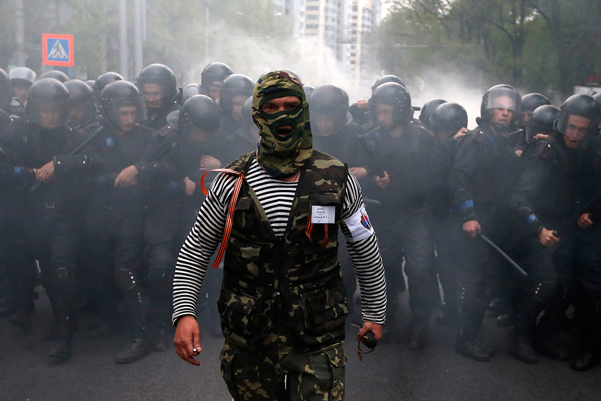 A pro-Russian protester walks in front of riot police during a pro-Ukraine rally in the eastern city of Donetsk. Several people were wounded when what appeared to be stun grenades exploded during a rally in support of Ukrainian unity.