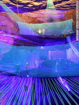 Multicolored LEDs cast eerie bouncing shadows on the rock walls as berserk grownups in prison inmate outfits bounce, hop and tumble along flimsy net chutes.