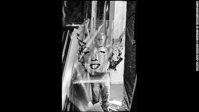 Artist Andy Warhol stands in the doorway of his studio, the Factory, in 1964, holding the acetate he used to make his famous Marilyn Monroe paintings. Warhol's work centered on famous personalities and iconic American objects, making him a leading figure in the pop art movement. 
